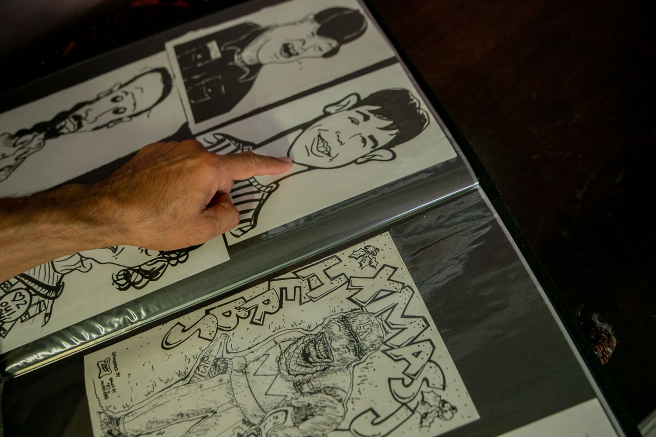 services-01 Close-up of a hand pointing at caricature sketches in an art portfolio on a dark surface.