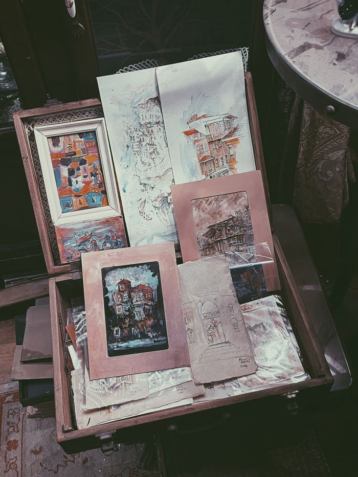 about-us-01 An open suitcase filled with vintage artworks and sketches in a retro, artistic setting.