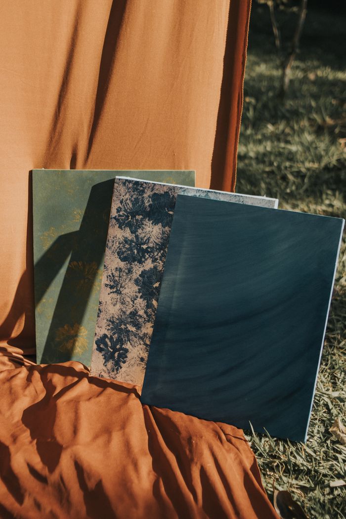 heros-img Three artistic textured canvases displayed outdoors against an earthy backdrop.