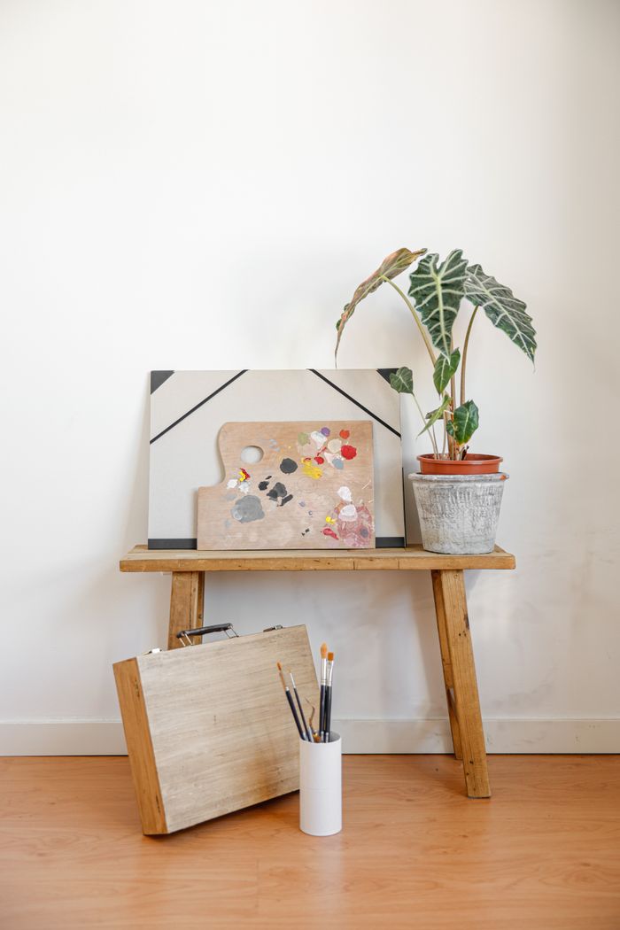 services-02 Minimalist creative workspace featuring painting tools, canvas, and a potted plant on a wooden bench.